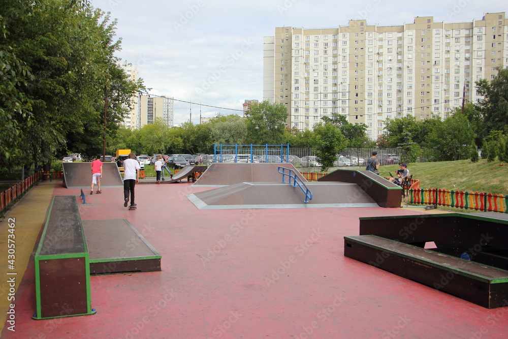 Modern outdoor urban skatepark with skateboarders on ramps in Moscow district Nagatino at Sunny summer day, Russian extreme youth people city sports in Park on multi-storey houses background view