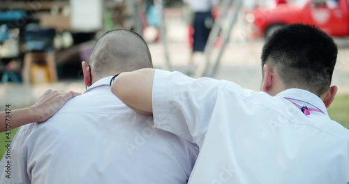 Two male Asian high school students in white uniform who are close friends waiting for the school shuttle or waiting for their parents to pick them home in the evening after school. photo