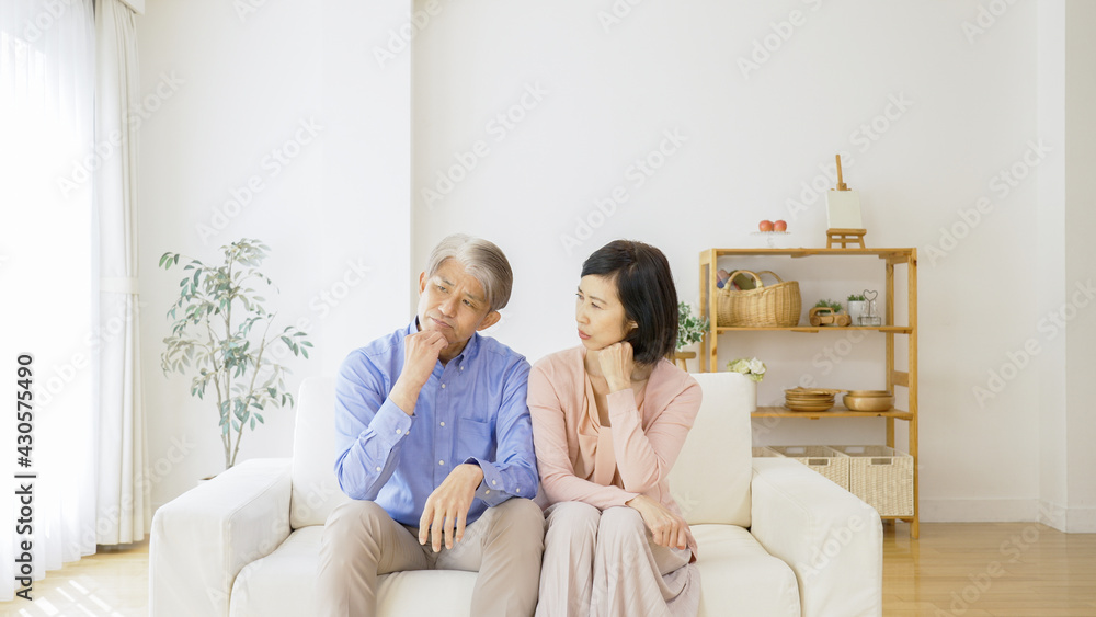 リビングで考え事をする中高年夫婦 リビングで考え事をする中高年夫婦