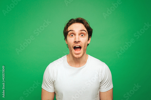 Young man looks surprised about news, isolated on green background