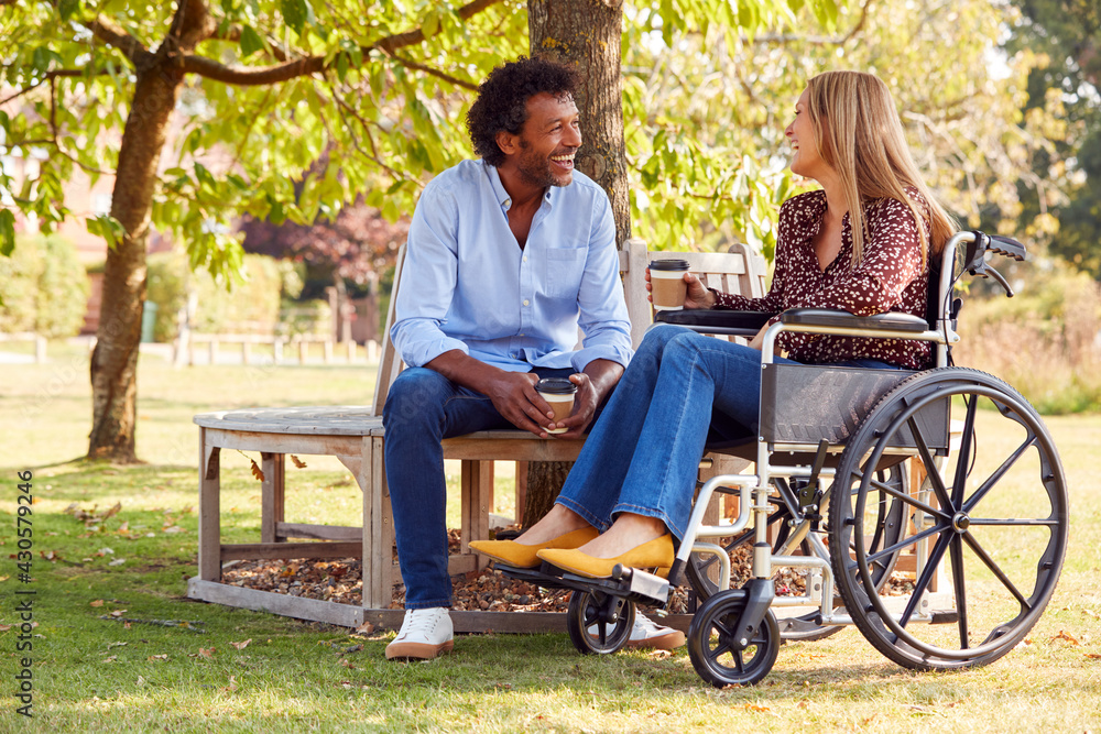 Mature Couple With Woman Sitting In Wheelchair Talking And Drinking Coffee In Park Together Mature Couple With Woman Sitting In Wheelchair Talking And Drinking Coffee In Park Together