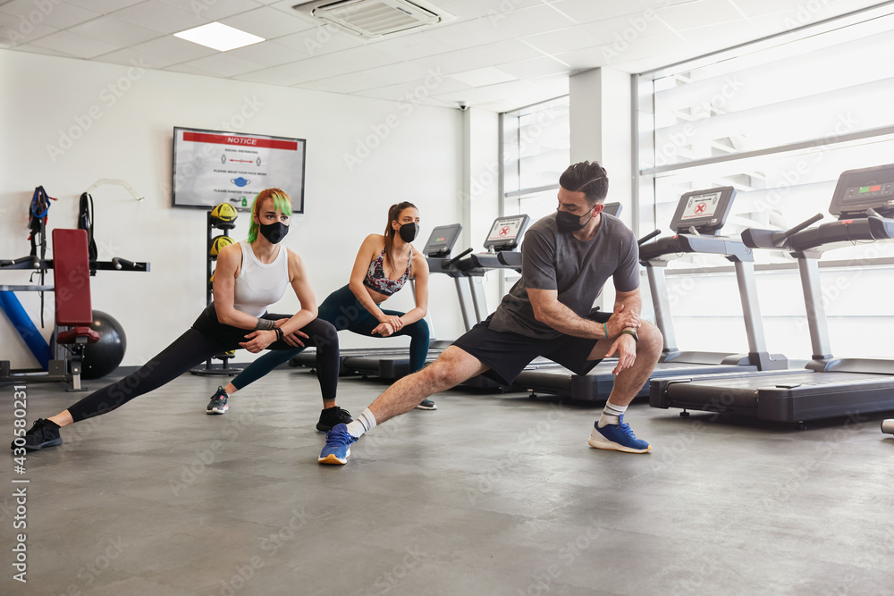 Healthy fit group of people stretching, wearing masks in gym