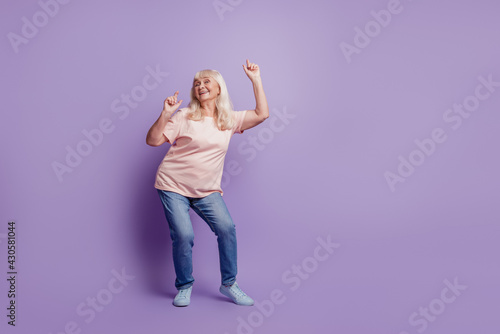Mature cheerful grey haired lady dancing on purple background