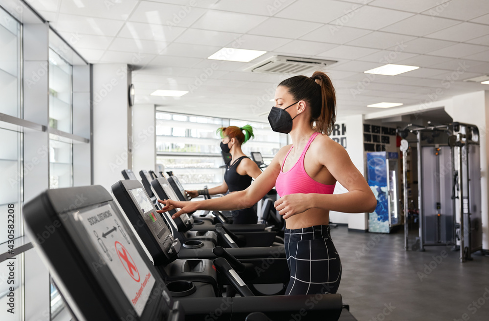 Two fit women exercising on treadmill wearing face mask in gym during pandemic