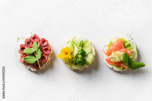 Rice crispbread with different toppings of vegetables, berries and red fish on white background. Flat lay. View from above. Healthy food snack. Tasty summer appetizer.