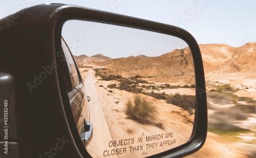 Side mirror of a driving car in the desert with text saying "objects in mirror are closer than they appear"