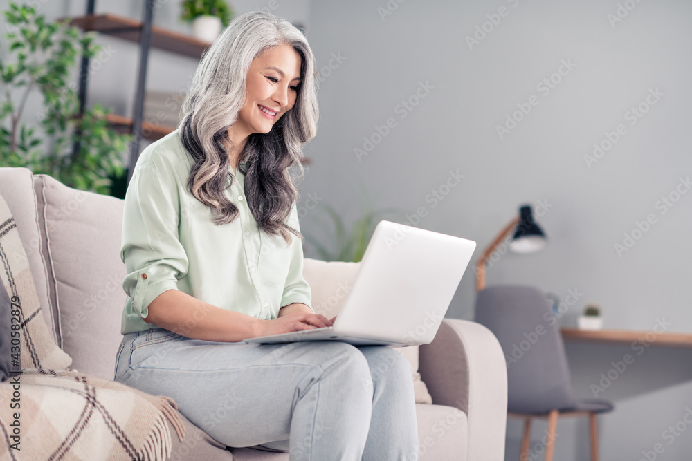 Photo portrait of elder woman sitting on sofa using laptop reading information Photo portrait of elder woman sitting on sofa using laptop reading information