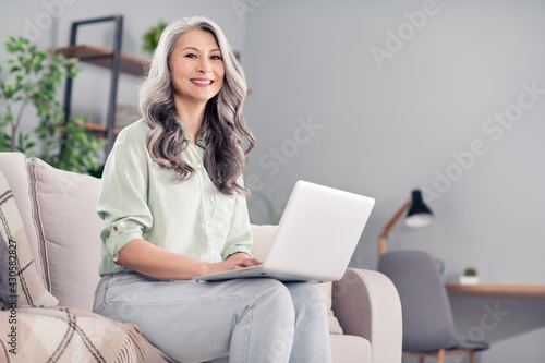 Photo portrait of elder woman sitting on sofa typing message on computer in social media