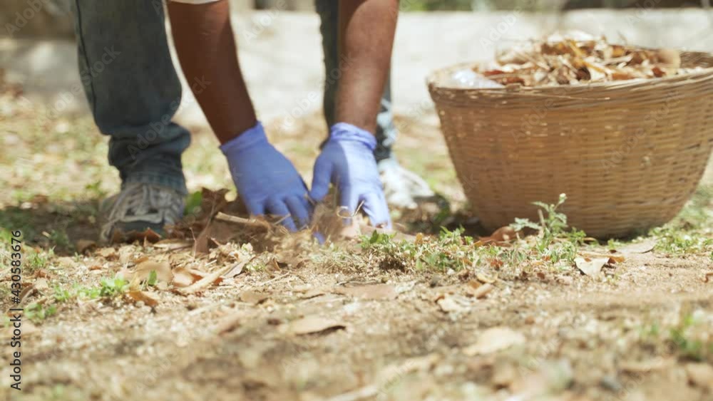 unrecognizable volunteer worker cleaning leaves and collecting inside the round bamboo basket while sweeping. unrecognizable volunteer worker cleaning leaves and collecting inside the round bamboo basket while sweeping.