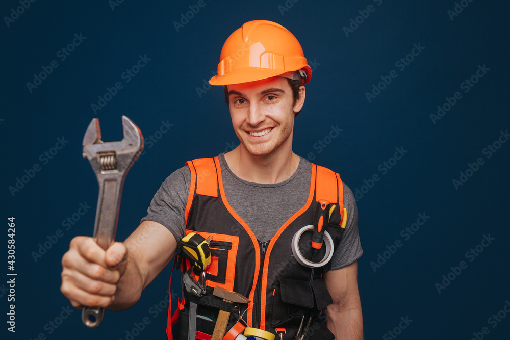 Smiling builder in a helmet is holding wrench, isolated over blue background Smiling builder in a helmet is holding wrench, isolated over blue background