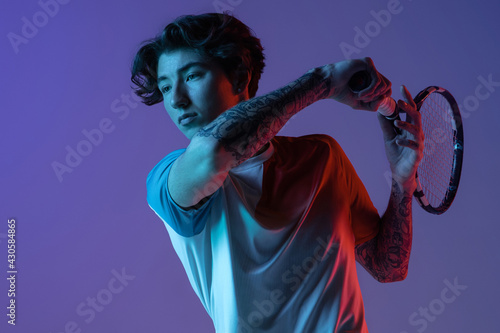 Young caucasian man playing tennis isolated on purple-blue studio background in neon, action and motion concept