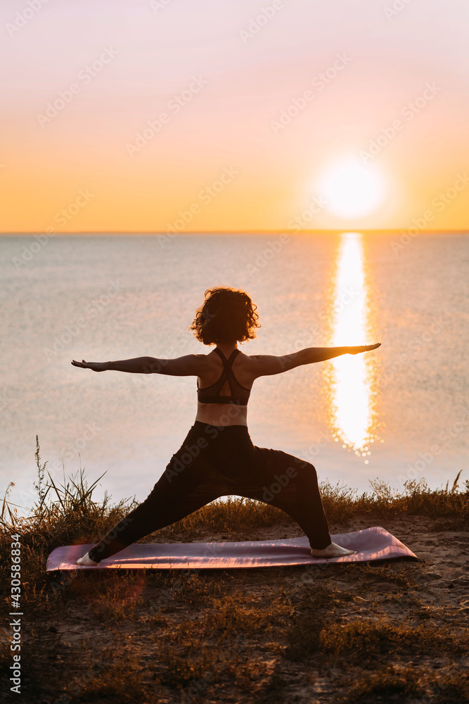 Vertical Yogi woman practices yoga at sunrise by the sea. Finding balance. Positive attitude, balance.