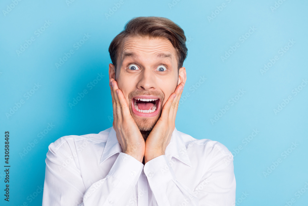 Photo of scared unhappy young man hold hands cheeks news unexpected isolated on blue color background Photo of scared unhappy young man hold hands cheeks news unexpected isolated on blue color background