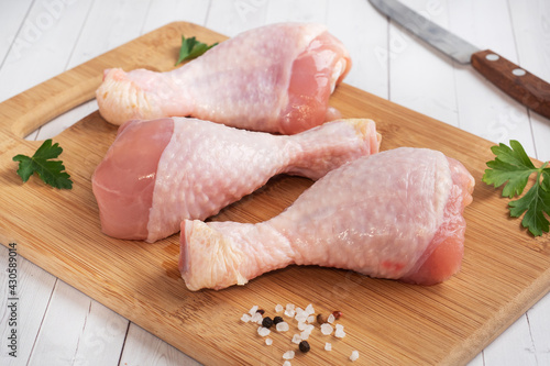 Raw chicken drumsticks with parsley and spices on a wooden cutting Board.