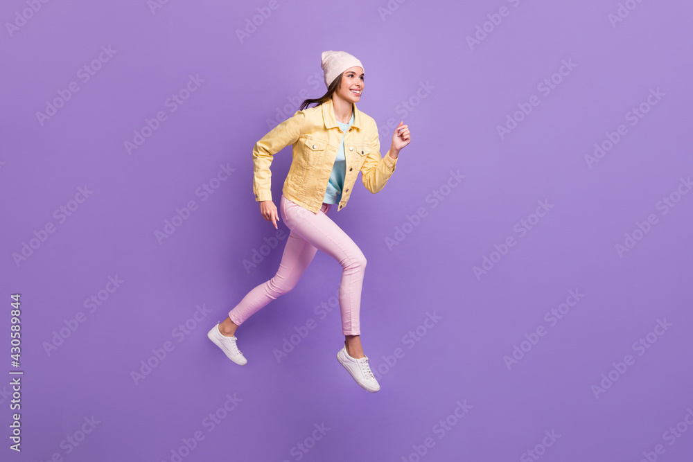 Full length body size photo of smiling woman jumping running fast looking empty space isolated on vivid purple color background Full length body size photo of smiling woman jumping running fast looking empty space isolated on vivid purple color background