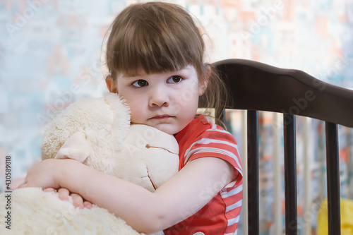 A small, sad girl sits, hugs a soft plush toy and misses her mother. A serious child with a toy at home. A thoughtful child. The child plays alone. The concept of parental inattention to the child