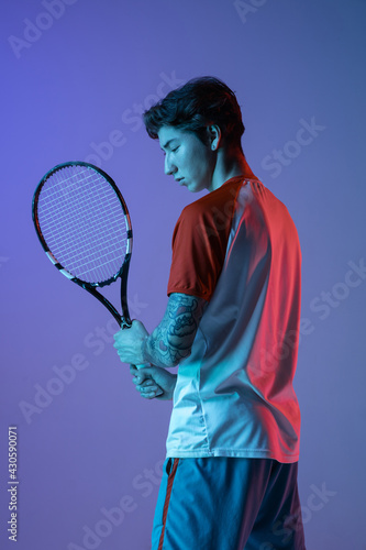 Young caucasian man playing tennis isolated on purple-blue studio background in neon, action and motion concept © master1305