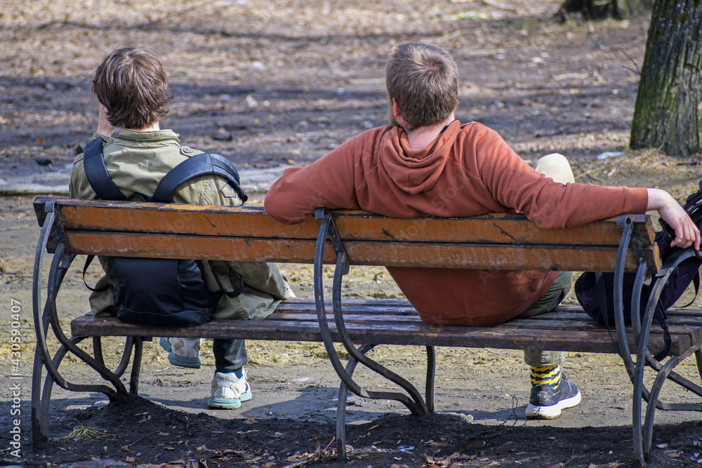 Two young guys sit on a bench in a city park Two young guys sit on a bench in a city park
