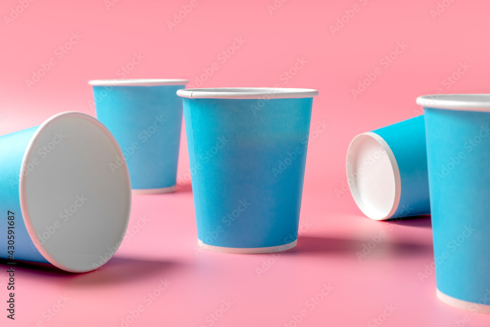 Disposable paper cup randomly and orange juice on a pink background. Disposable tableware. Disposable goods. Concept. Disposable paper cup randomly and orange juice on a pink background. Disposable tableware. Disposable goods. Concept.