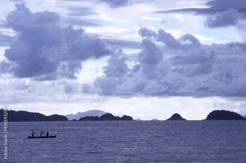 Three fishermen on the boat and some islands behind 