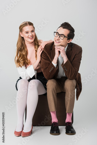 cheerful woman leaning on shoulder of boyfriend while sitting on suitcase on grey background © LIGHTFIELD STUDIOS