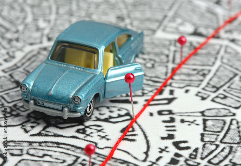 City map, route marked with safety pins. The blue toy car stands with the door open. Concept: travel along the route, stopover, destination, goal. City map, route marked with safety pins. The blue toy car stands with the door open. Concept: travel along the route, stopover, destination, goal.