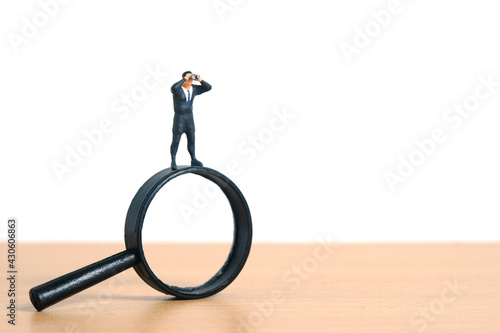 Businessmen standing using binoculars above magnifying glass. Miniature tiny people toys photography. isolated on white background.