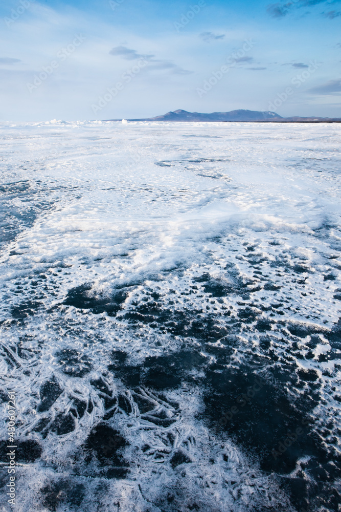 Thin snow forms whimsical patterns on the ice Baikal and mountains in the distance with the sky Thin snow forms whimsical patterns on the ice Baikal and mountains in the distance with the sky