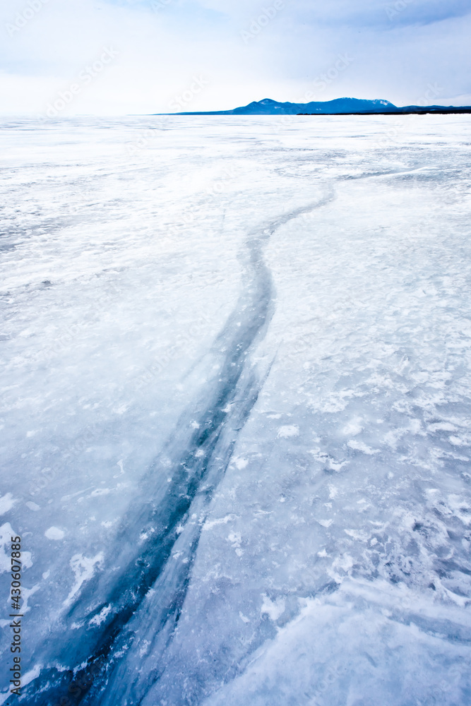 Blue crack stretching into the distance on Baikal with mountains and sky Blue crack stretching into the distance on Baikal with mountains and sky