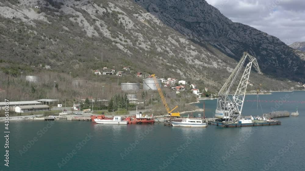 Flying over the sea towards the coast, to the industrial pier, where there is a ship's crane and industrial transport - boats and ships Flying over the sea towards the coast, to the industrial pier, where there is a ship's crane and industrial transport - boats and ships