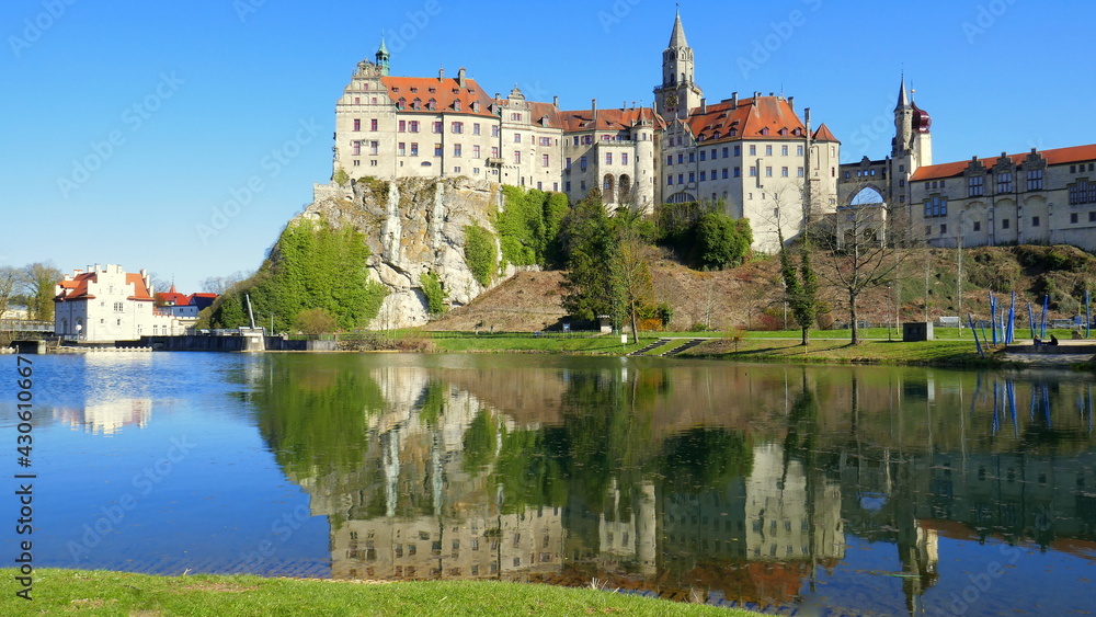 herrliches Schloss Sigmaringen spiegelt sich unter blauem Himmel vor grünen Ufer der Donau  mit Wehr