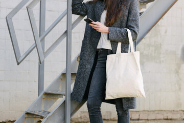 Woman holding white textile tote eco bag in urban area. Ecology or environment protection concept. White eco bag for mock up.