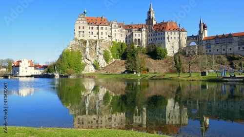 herrliches Schloss Sigmaringen spiegelt sich unter blauem Himmel vor grünen Ufer der Donau mit Wehr