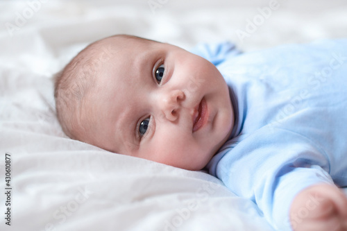 Close-up Portrait of a beautiful Baby on white. Head and Face. Newborn Baby lying on its side and looks into the Camera. Motherhood, health, pediatrics concept. Cute adorable Infant.