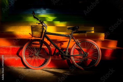 Black bicycle parked on colored stairs. Old bicycle with red tires and basket in front.