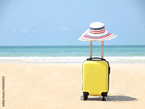 Travel on Summer and tourist planning with yellow suitcase with white hat fashion in the beautiful beach. Travel in holiday. Blue sky and sand background  on travel in summer concept.