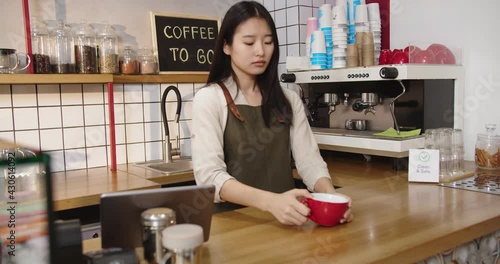 Beautiful female barista amking coffee, taking cup and putting it on bar table in cafe. Young Asian woman holding beverage, looking at camera and smiling. Clean Safe. Service, part-time job concept. photo