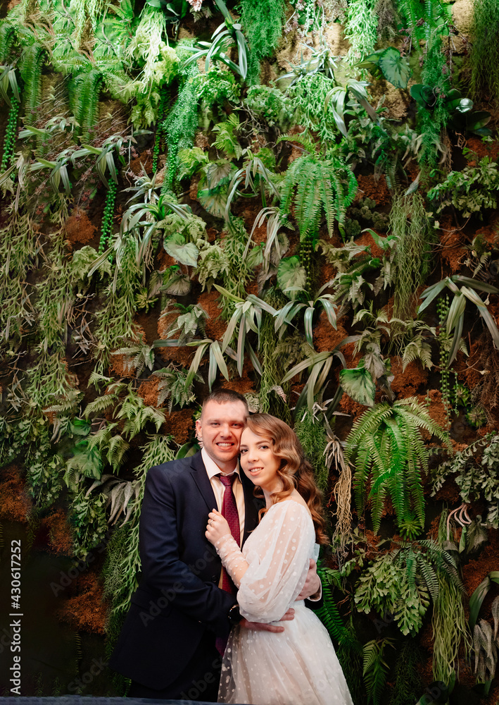 Obraz premium happy bride and groom at the wall decorated with live plants.