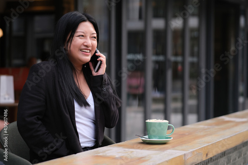 portrait of smiling Asian young woman making phone call at outdoor cafe with a cup of coffee
