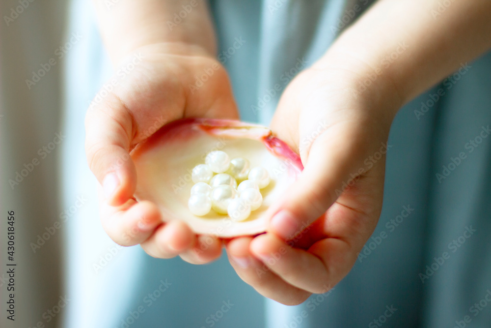 Children's hands hold oyster shell with pearls Children's hands hold oyster shell with pearls