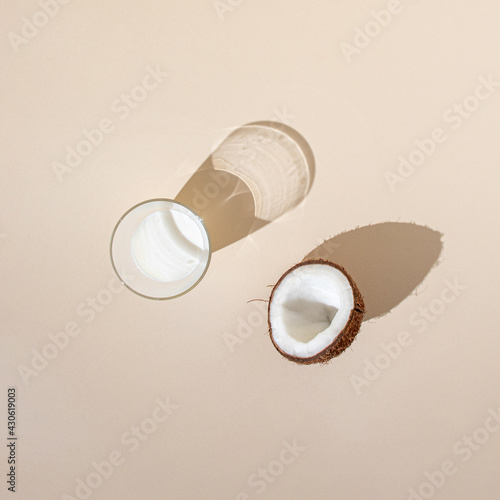 half of fresh coconut with coconut milk in the glass on the bright cream background. minimal creative decoration summer idea