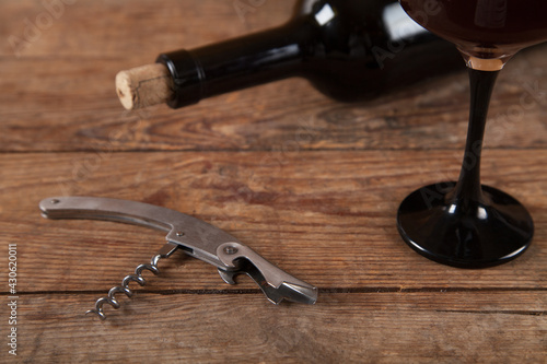 Bottle, glass and wine with corkscrew on wooden background.