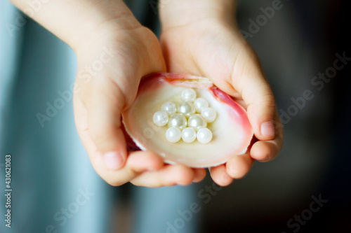 Children's hands hold oyster shell with pearls	