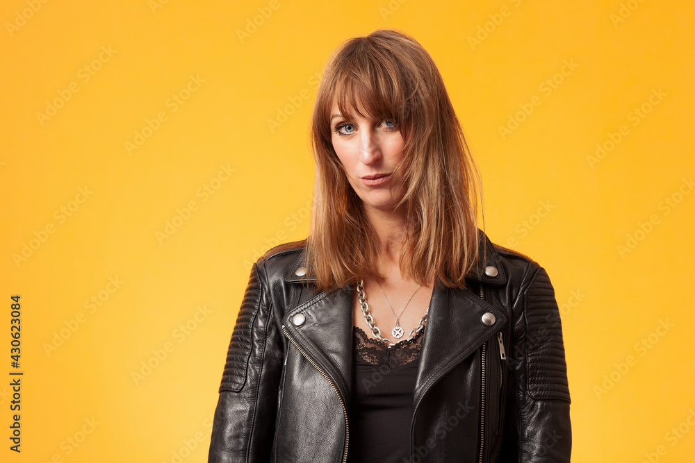 Titel: Portrait of an attractive woman wearing a black leather jacket against yellow background Titel: Portrait of an attractive woman wearing a black leather jacket against yellow background