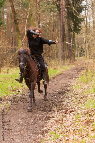 beautiful woman riding in historical costume as a warrior rides a horse and shoots an arrow from a bow