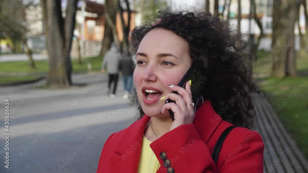 Beautiful young curly girl in a red coat is chatting on a smartphone in the city Beautiful young curly girl in a red coat is chatting on a smartphone in the city