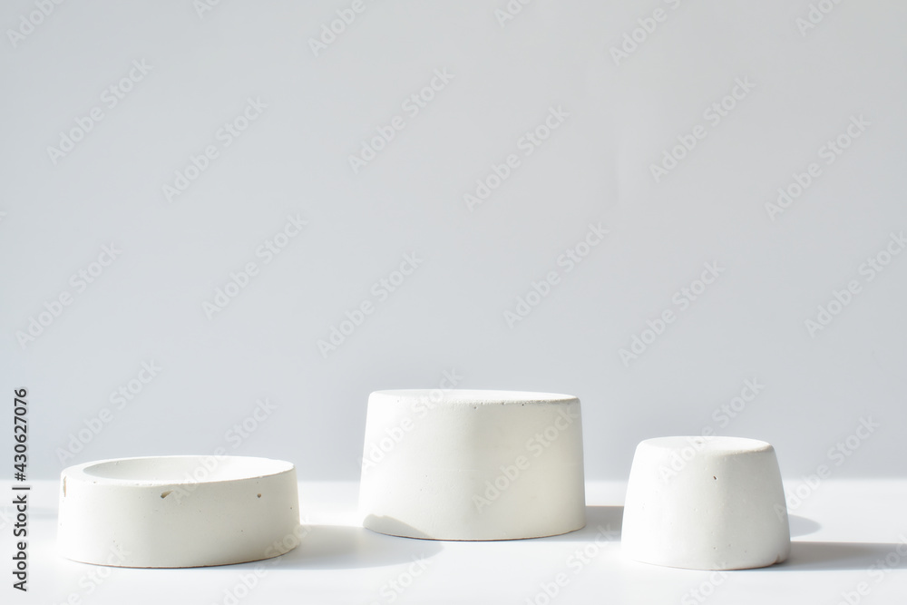 Three white catwalks with a geometric figure made of concrete. A scene with a cement display case. Minimalistic background. Presentation of cosmetics. Three white catwalks with a geometric figure made of concrete. A scene with a cement display case. Minimalistic background. Presentation of cosmetics.