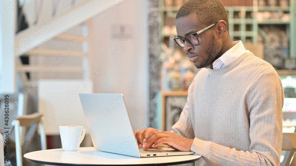 Focused African Man Working on Laptop in Cafe Focused African Man Working on Laptop in Cafe