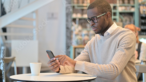 Attractive African Man using Smartphone in Cafe 