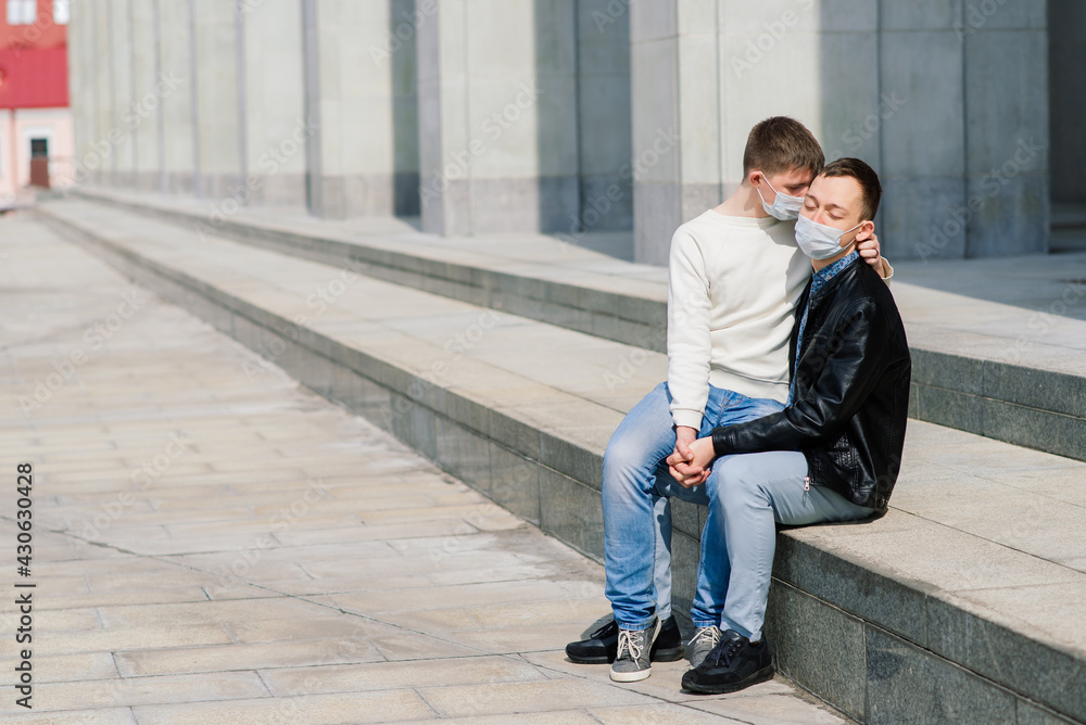 Young gay couple wearing medical mask, hugging and kissing at the city.